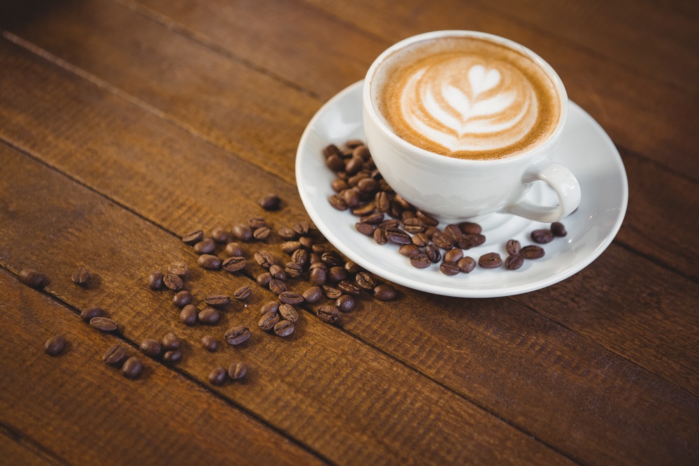 Cup of cappuccino with coffee art and coffee beans on wooden table.jpeg