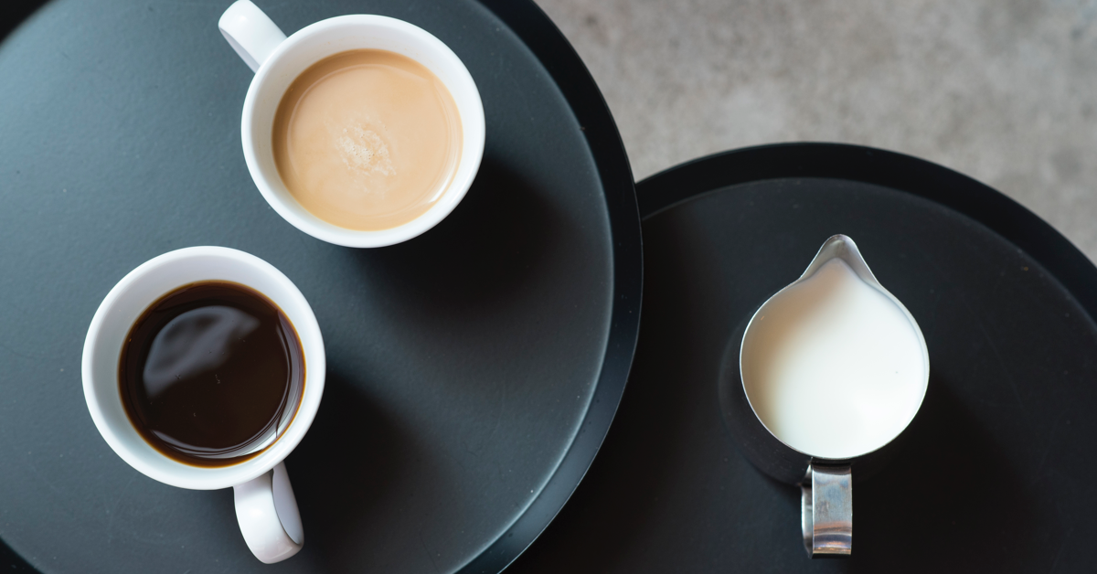 To runde bord. end to kopper kaffe og en kanne melk. guide til kaffe på jobben.