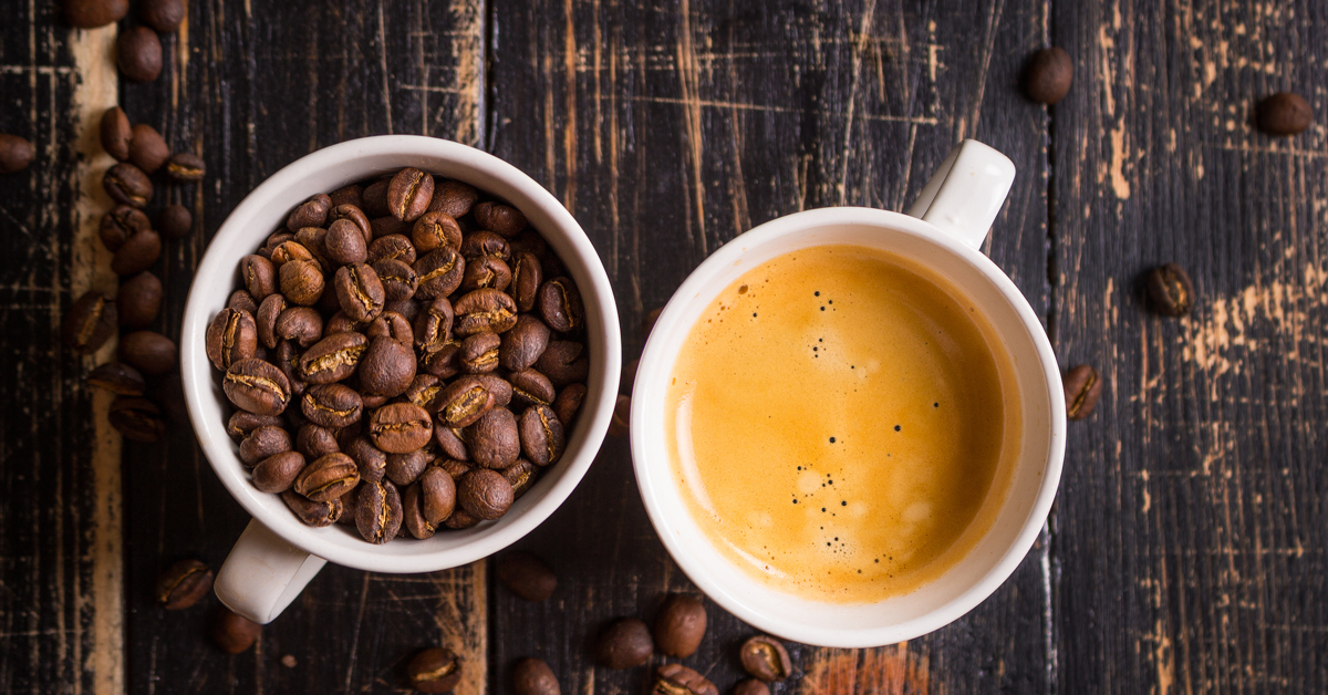 En kopp med kaffebønner og en kopp med kaffe på en brun treplate. Guide til kaffe på jobben.