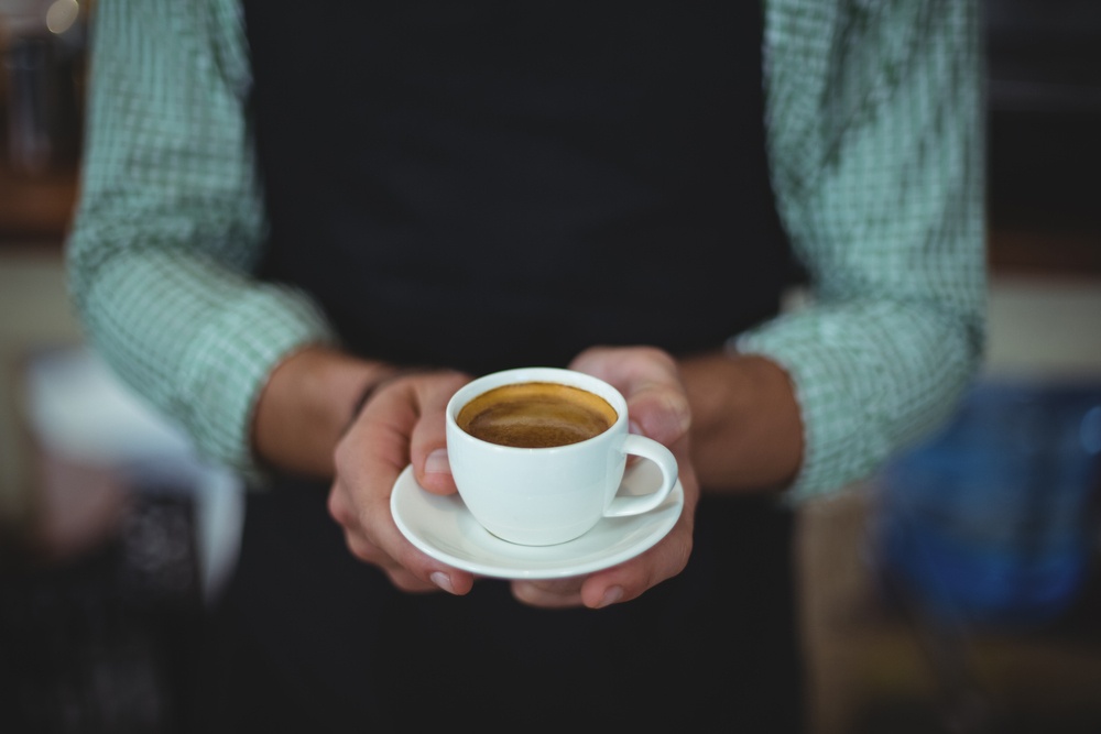 Mid section of waiter holding cup of coffee in cafe.jpeg