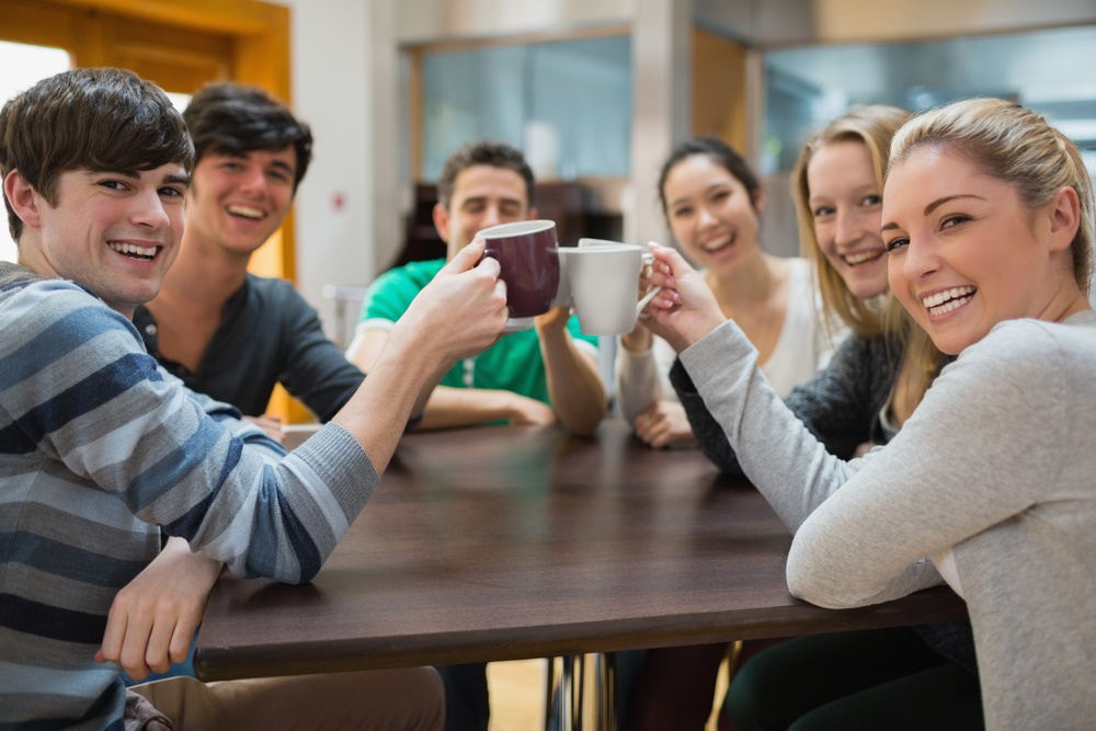 Students sitting clinking cups while smiling in college cafe.jpeg