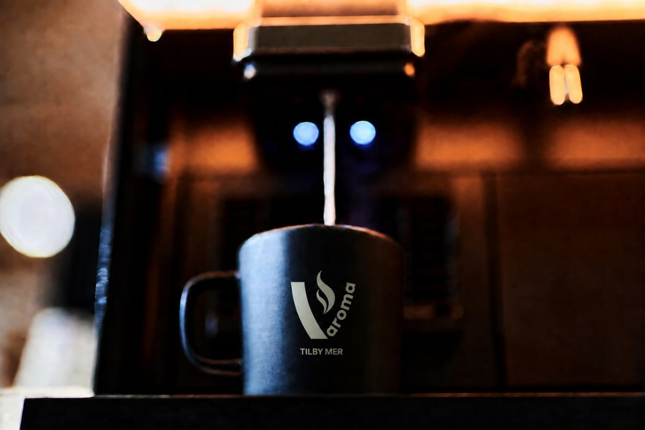 Kopp med v:aroma-logo og tilby mer under maskinen i varmt lys