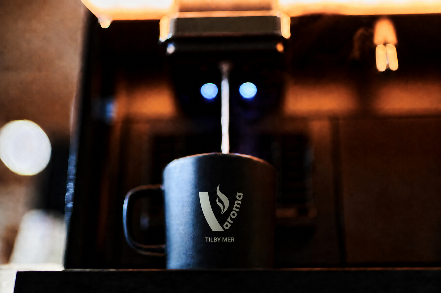 Kopp med v:aroma-logo og tilby mer under maskinen i varmt lys