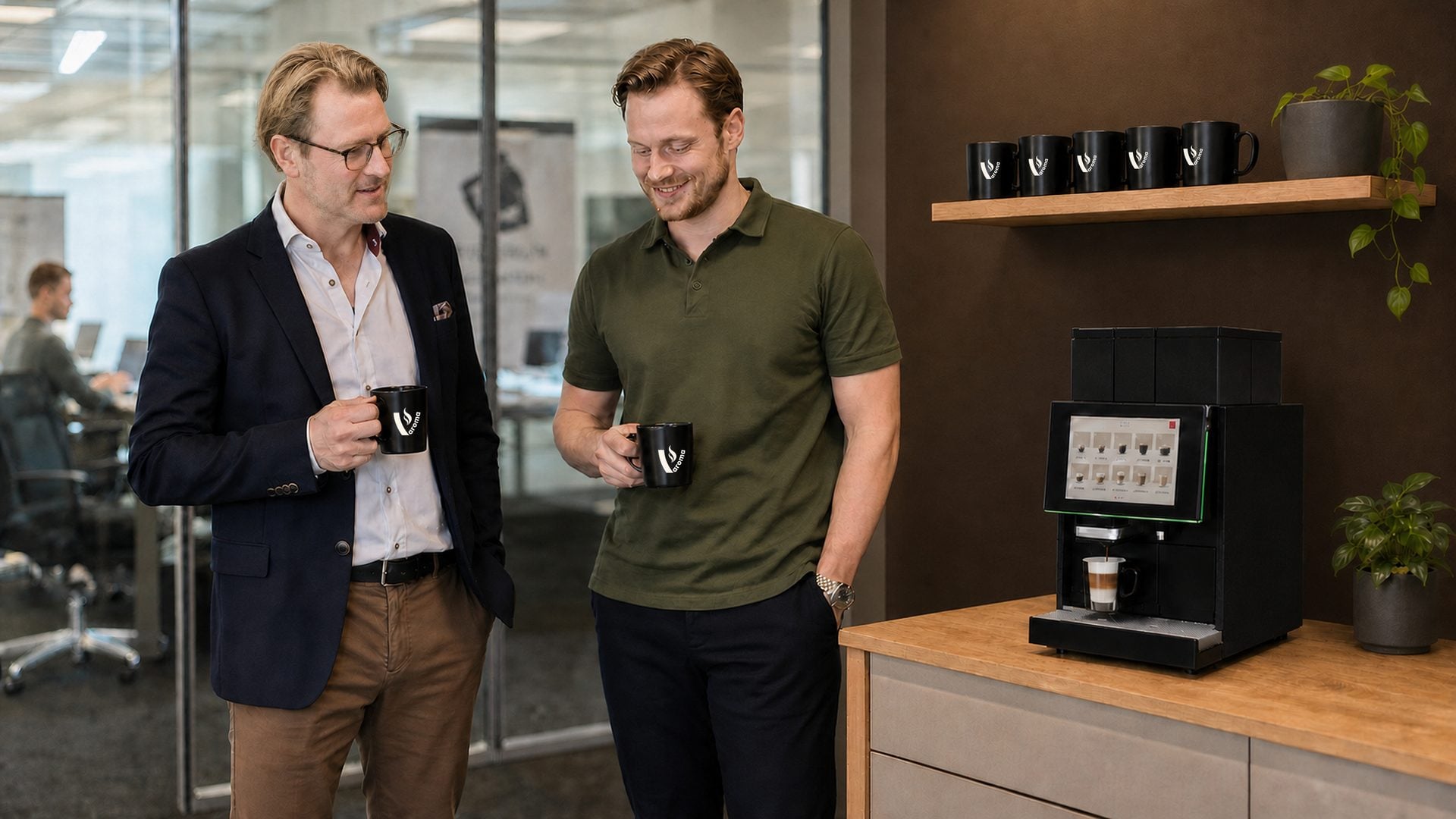 To kollegaer med kaffekopper ved kaffemaskinen på et kontorkjøkken